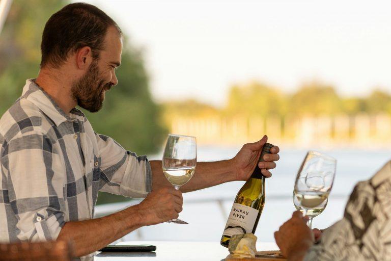 Homme tenant un verre de vin blanc, contemplant une bouteille de vin blanc avec le sourire.