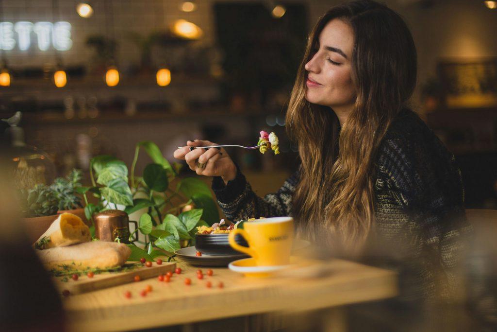 Femme mangeant une salade de pâtes au fromage les yeux fermés dans un restaurant.